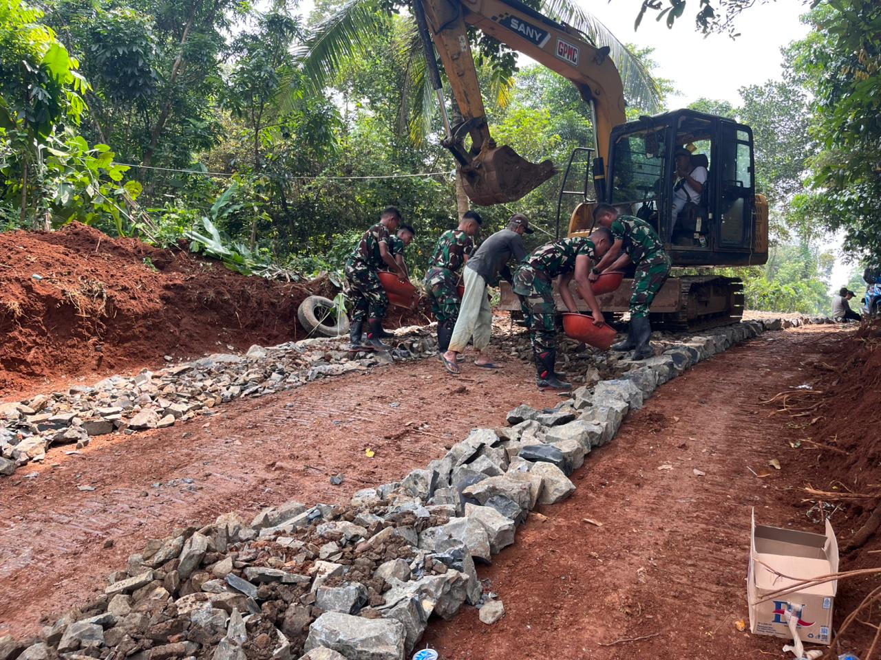 Satgas TMMD Ke-126 Kodim 0601/Pandeglang Lanjutkan Pengerasan Jalan dengan Bantuan Alat Berat Ekskavator, Batu Disebar untuk Dasar yang Kokoh